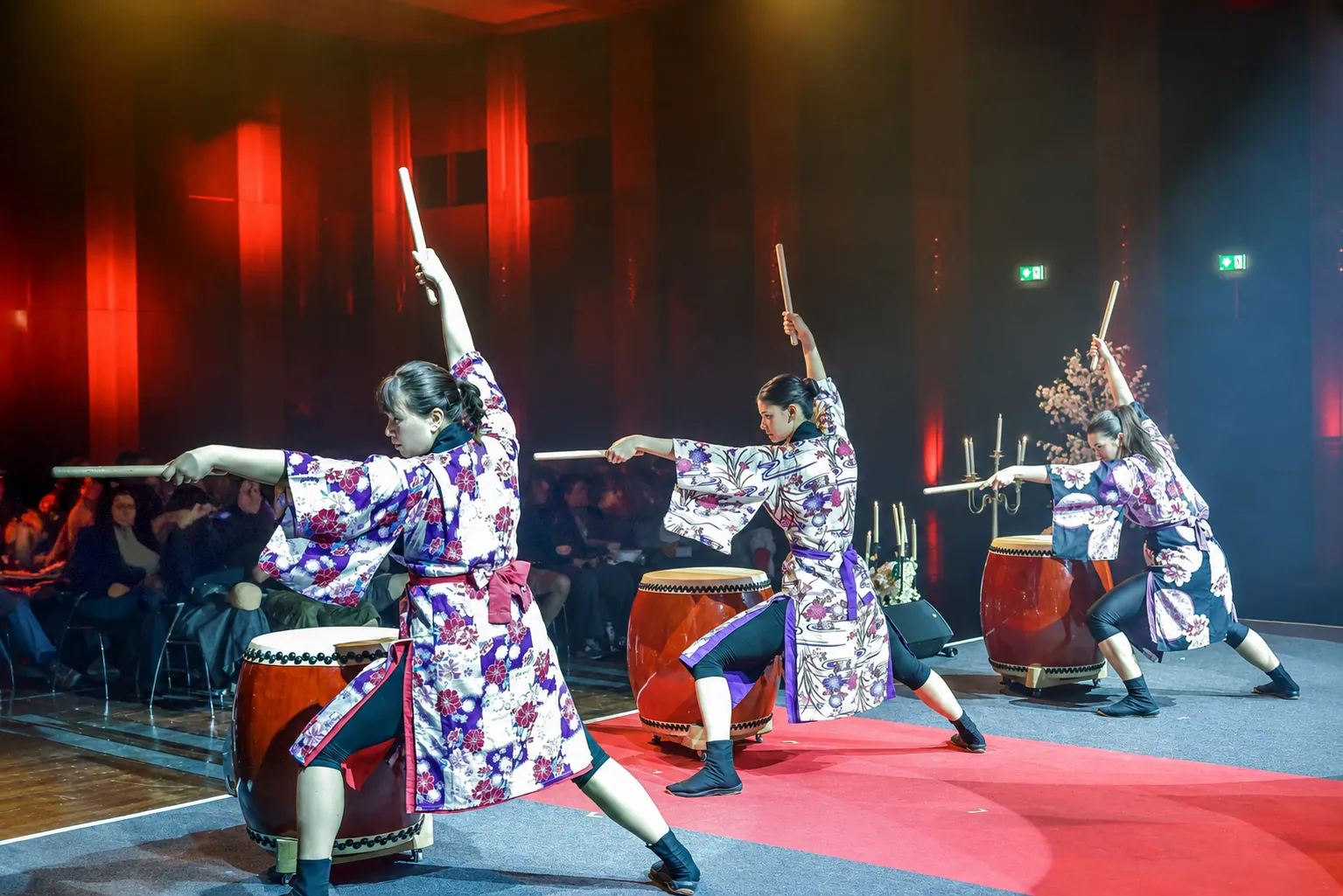 Three members of Taiko LION in patterned kimonos performing together on drums